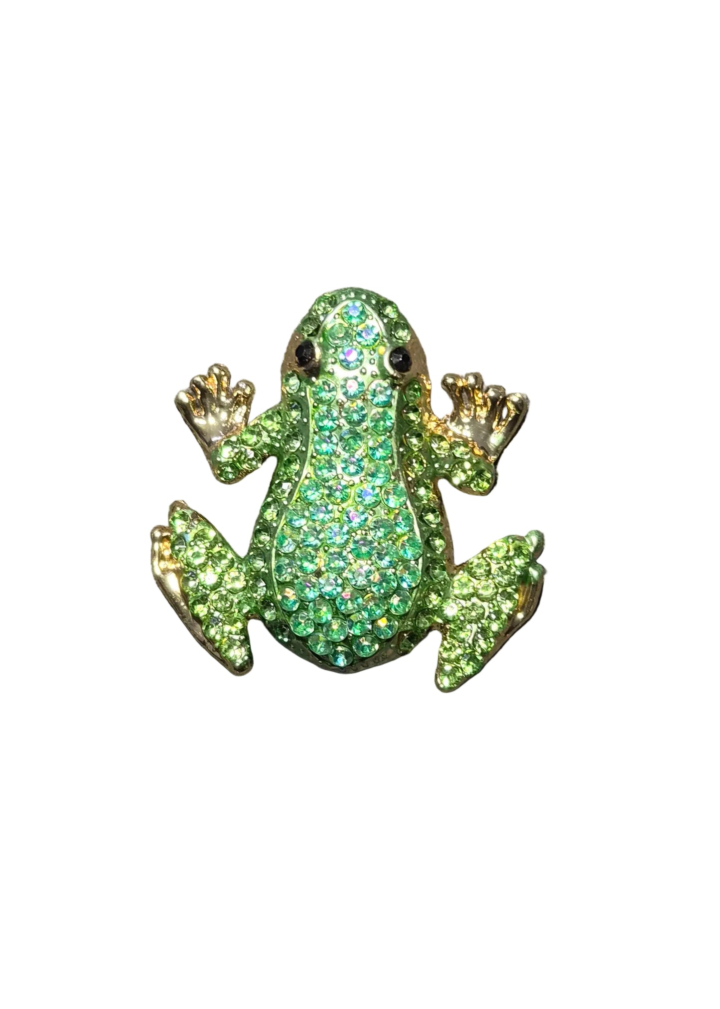 A small frog-shaped brooch or pin covered in green rhinestones with gold-tone edges and black eyes, placed on a dark gray textured fabric surface.