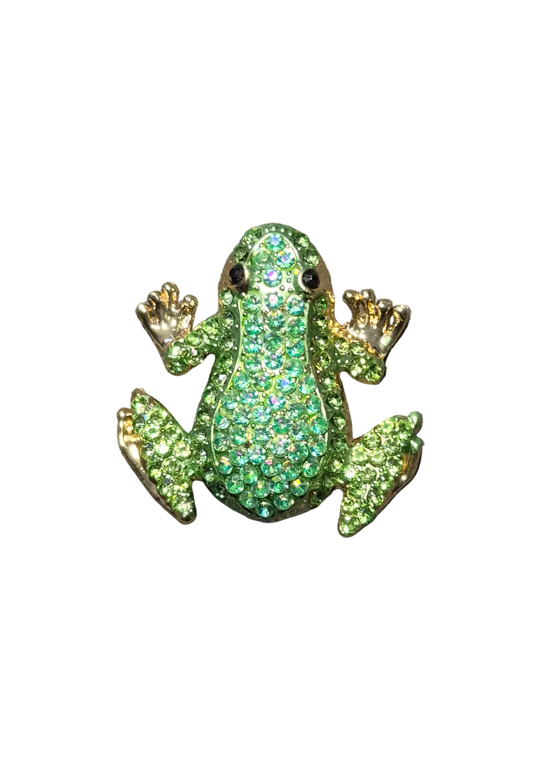 A small frog-shaped brooch or pin covered in green rhinestones with gold-tone edges and black eyes, placed on a dark gray textured fabric surface.