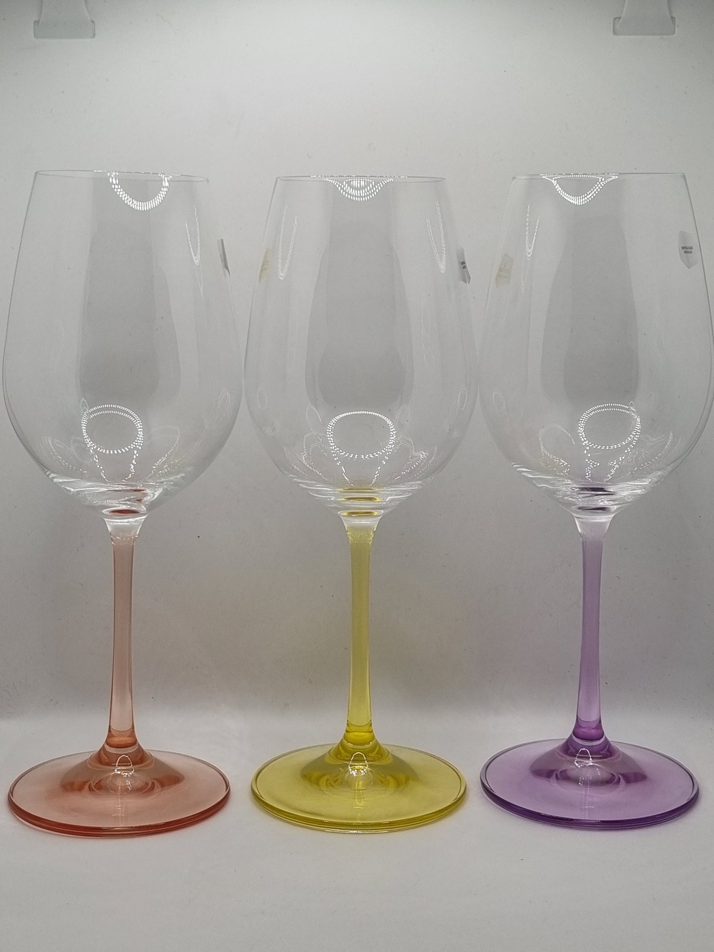 Set of three white wine glasses with red, purple and yellow stems on a light grey background