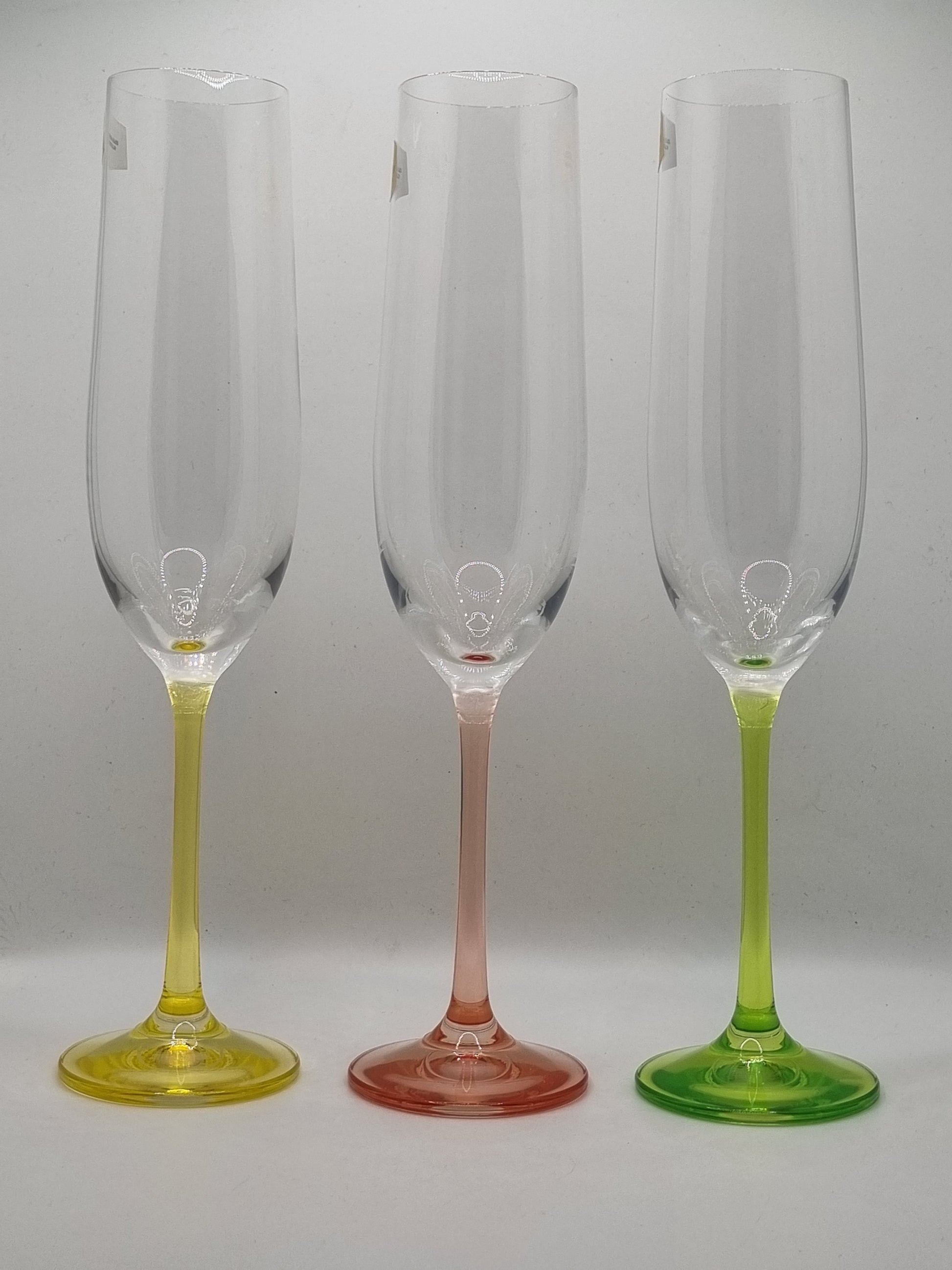 Set of three champagne flutes with yellow, red and green stems on a light gray background
