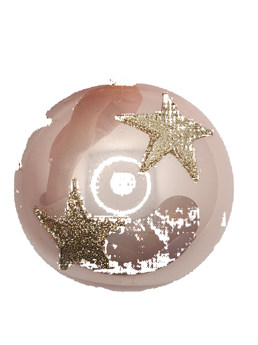 Pink decorative ball with gold stars held by a hand against a white background